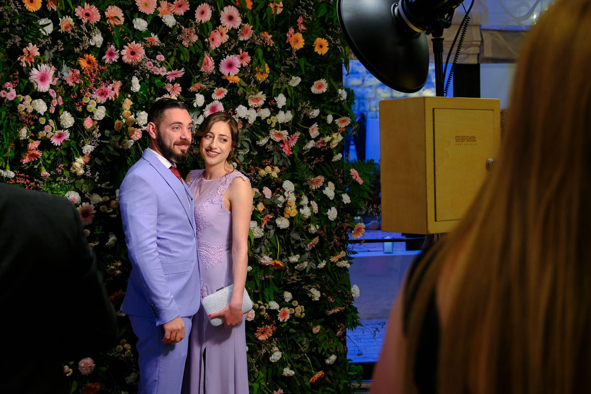 A couple posing in a vintage photo booth with a live flower wall
