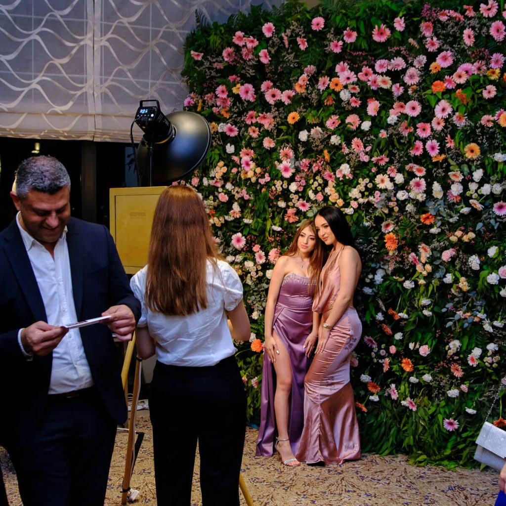 Ladies posing against a live flower wall in front of a vintage photo booth