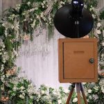 A custom flower arch being used as a backdrop with a vintage photo booth