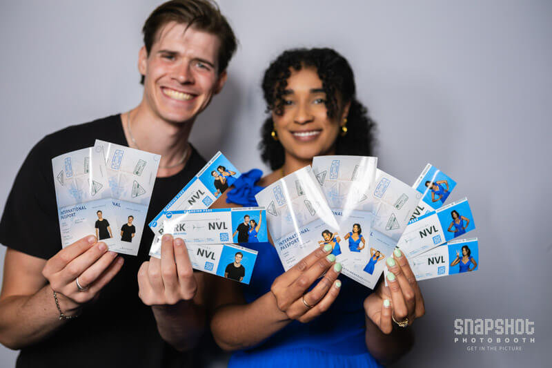 two people holding up samples of boarding pass and passport prints from a travel Photo Booth