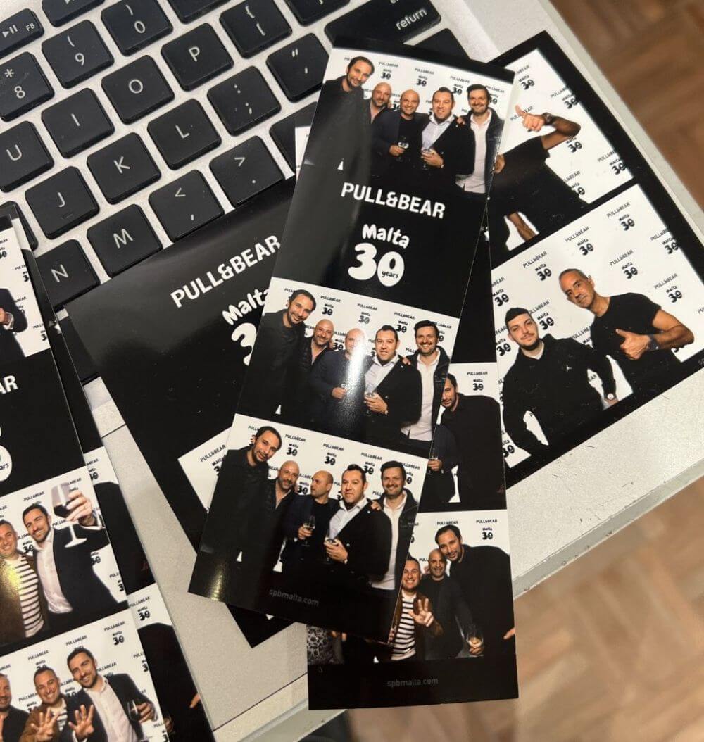 pull-and-bear-malta-30th-anniversary-photo-strips-keyboard Printed photo strips placed on a laptop keyboard, showing groups posing in front of a “PULL&BEAR Malta 30 years” backdrop.