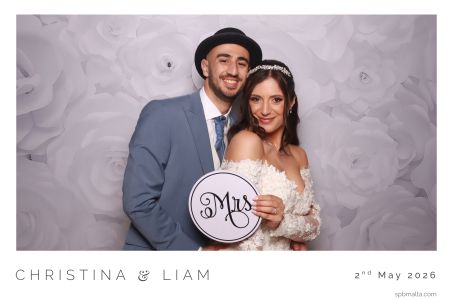 bride-groom-photo-booth-villa-overhills-malta he bride and groom posing with "Mrs" props in front of a white rose backdrop at Villa Overhills.