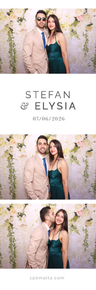 Stefan & Elysia-07 A wedding guest couple wearing sunglasses and kissing in front of a floral backdrop.
