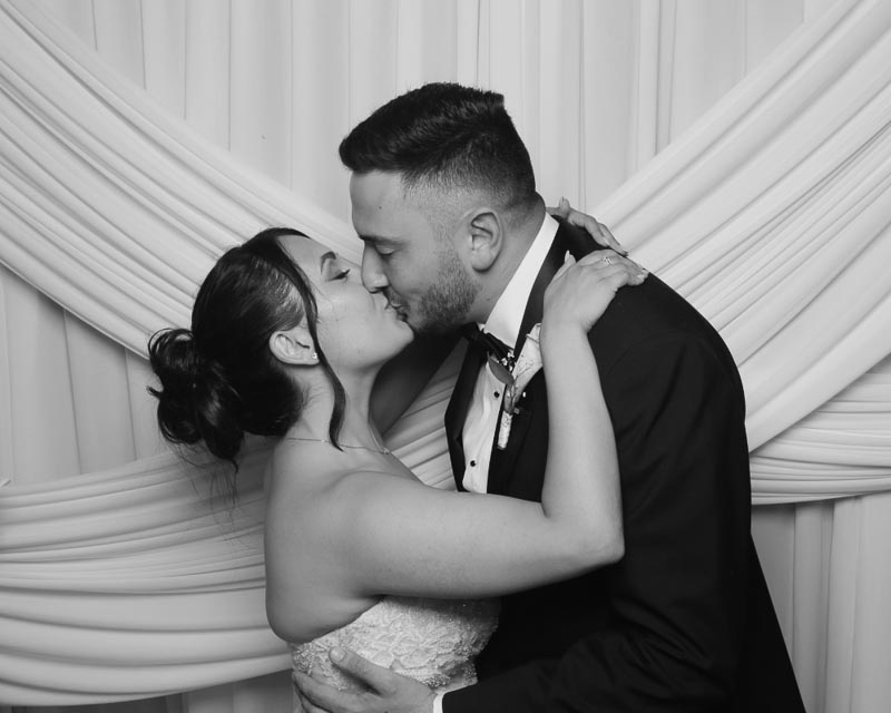 wedding-photo-booth-malta-newlyweds-taking-photos Groom kissing the bride in front of a white wedding backdrop during their high-energy reception at The Phoenicia Malta.
