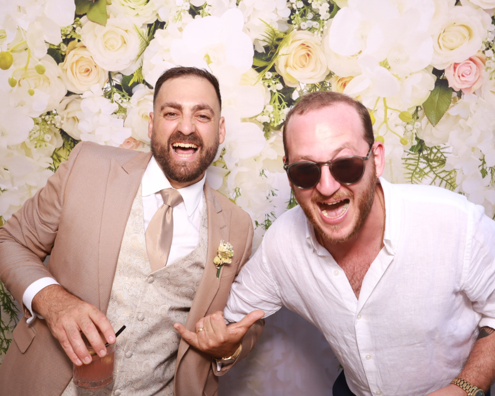 groom-with-friend-at-wedding-photo-booth Groom posing with a friend and capturing a fun wedding photo booth moment together.