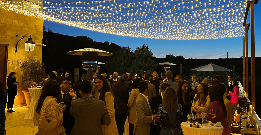 Wedding Reception Wedding guests mingle at dusk on a limestone terrace in Malta beneath a canopy of fairy lights and patio heaters.